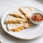 A plate of golden Chicken and Cheese Quesadillas served with a side of fresh salsa, placed on a marble countertop