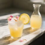 A glass of saffron rosewater lemonade with lemon slice and rose petals on a marble surface