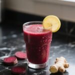 Fresh beet juice on black marble countertop with lemon and ginger