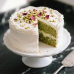 round pistachio milk cake topped with whipped cream and rose petals
