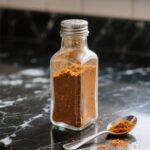 Taco seasoning in a glass spice bottle on black marble counter