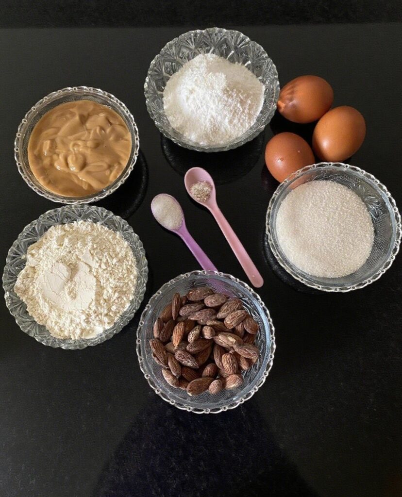 Ingredients for Almond Caramel Layer Cake, including eggs, cake flour, sugar, heavy cream, and caramel sauce, arranged on a wooden surface.