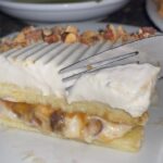 A close-up of a sliced Almond Caramel Layer Cake showcasing its golden sponge, caramel whipped cream, and toasted almonds.