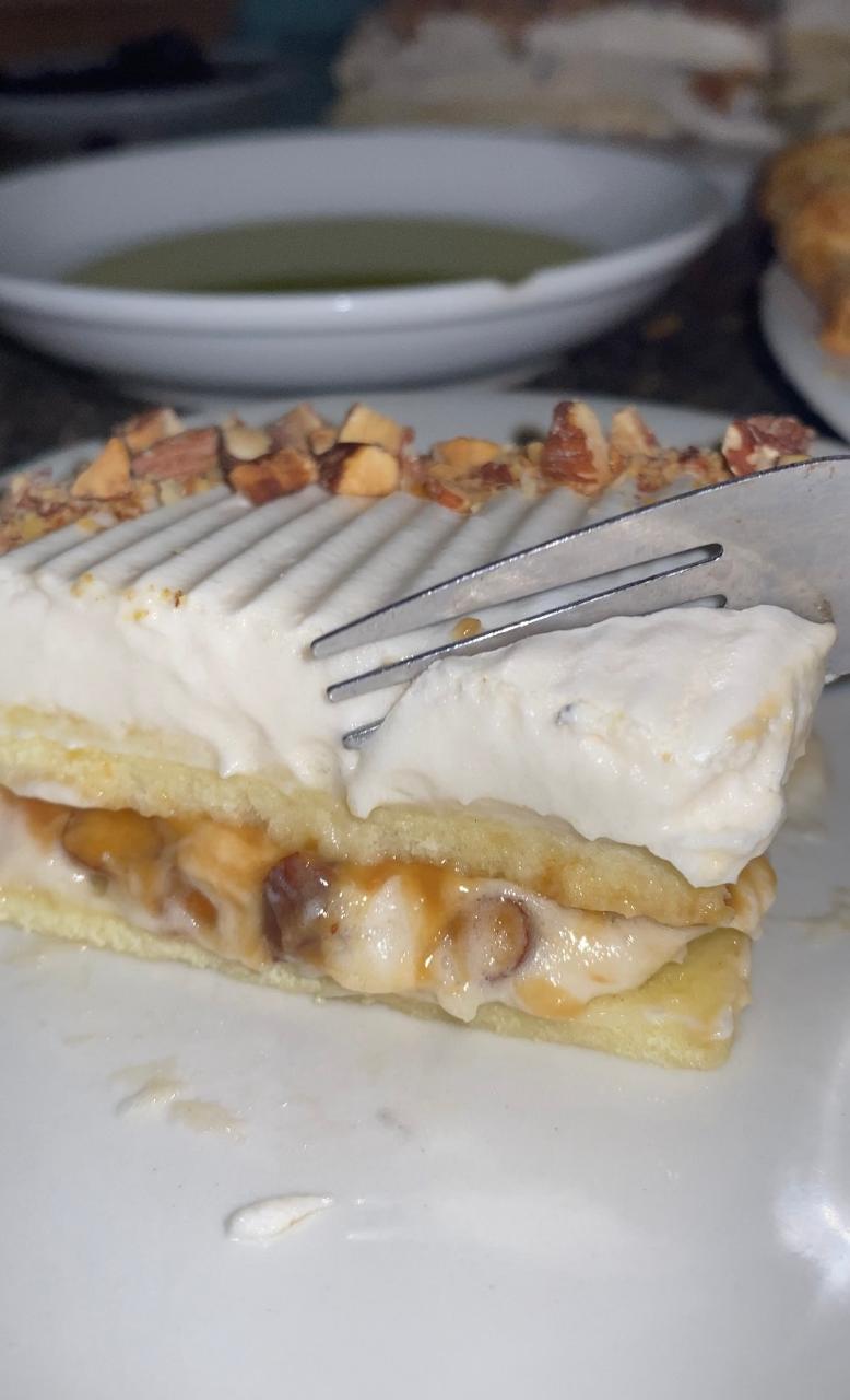 A close-up of a sliced Almond Caramel Layer Cake showcasing its golden sponge, caramel whipped cream, and toasted almonds.