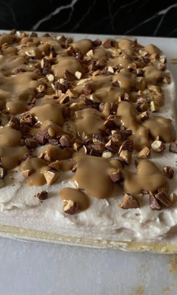 Assembling an Almond Caramel Layer Cake with caramel whipped cream, broken toasted almonds, and caramel drizzle.