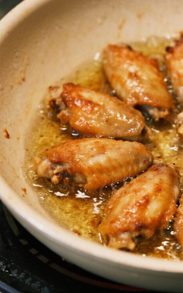 Whole30 crispy chicken wings frying in a skillet with hot oil, turning golden brown.