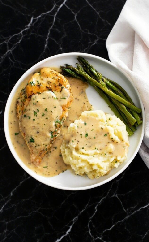 Final serving of Garlic Parmesan Chicken with creamy sauce, mashed potatoes, and roasted vegetables on a black marble countertop.