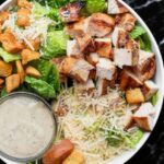 Grilled Chicken Caesar Salad with romaine lettuce, grilled chicken slices, croutons, parmesan, and Caesar dressing, served in a bowl.