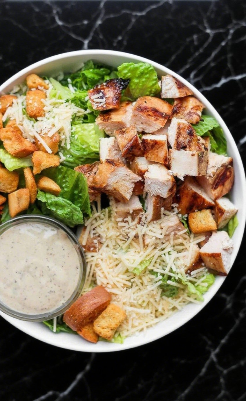 Grilled Chicken Caesar Salad with romaine lettuce, grilled chicken slices, croutons, parmesan, and Caesar dressing, served in a bowl.