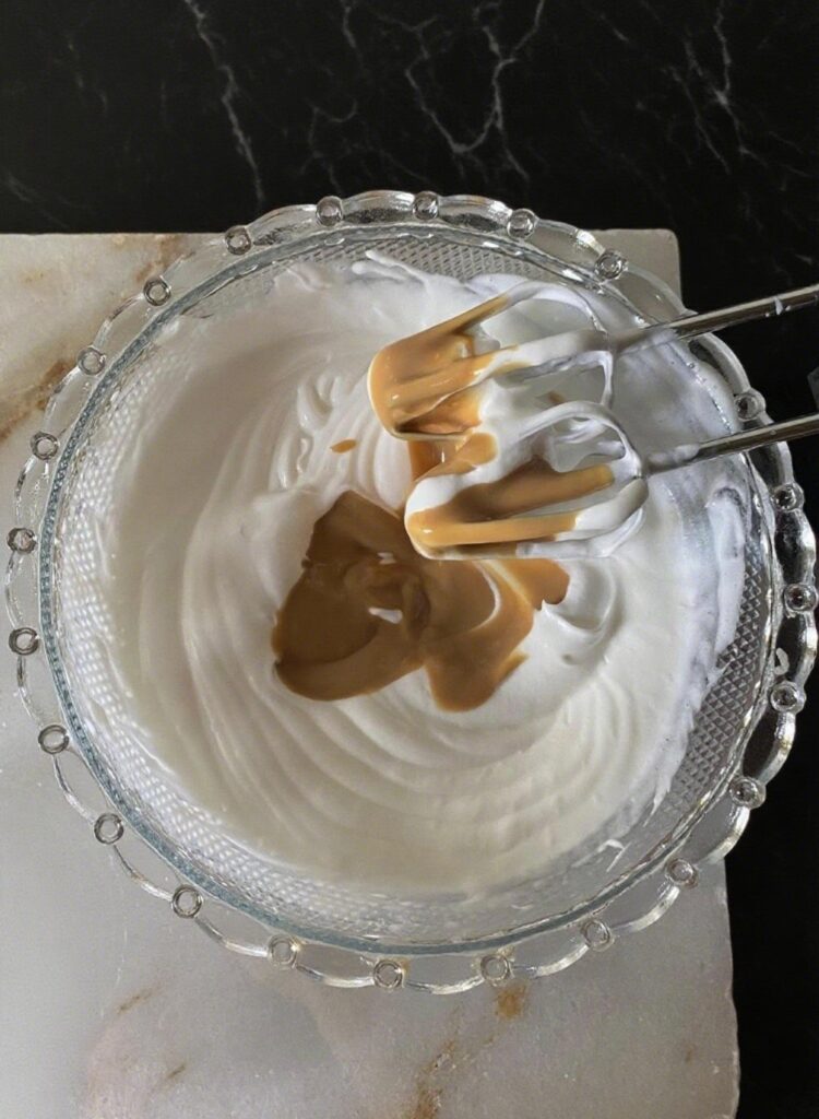 Close-up of whipped cream being mixed with caramel sauce, powdered sugar, and vanilla extract for an Almond Caramel Layer Cake.