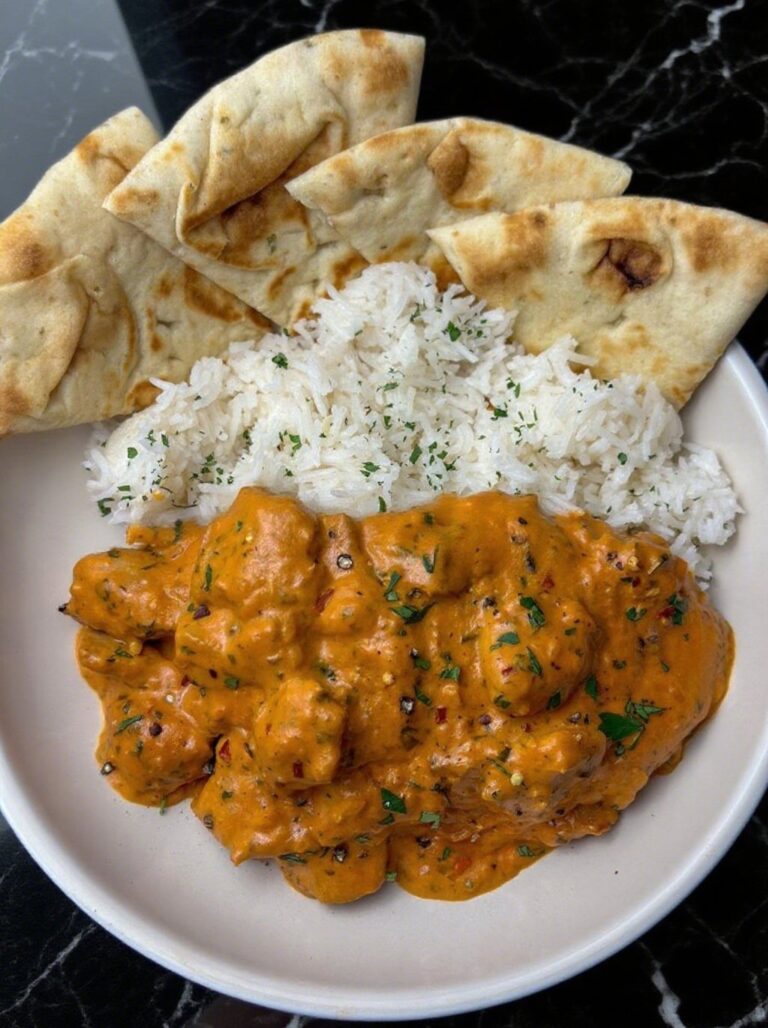 A plate of butter chicken with naan and rice, garnished with parsley, served in a rustic bowl.